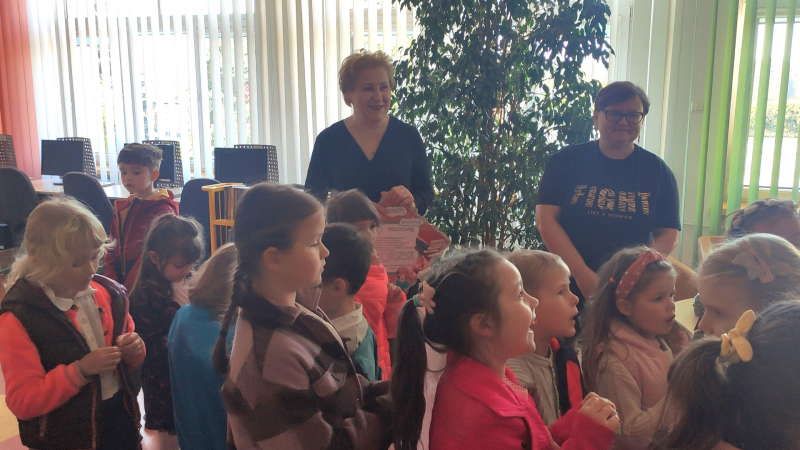 Zdjęcie kolorowe, przedszkolaki z życzeniami z okazji dnia bibliotekarza w bibliotece